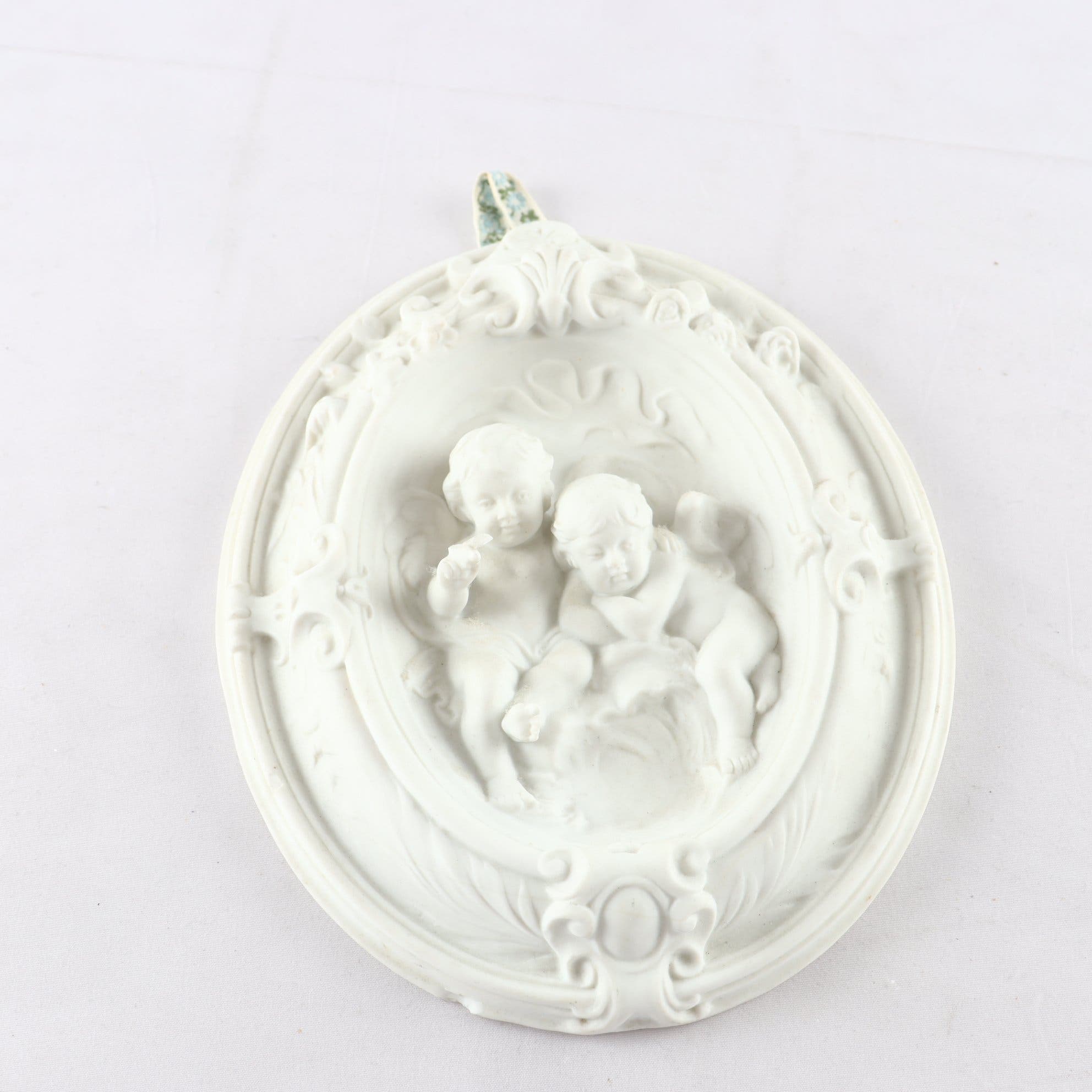 Väggplakett, parian, putti i relief. Samfraktas ej